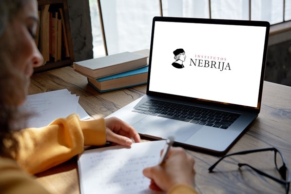 Chica sentada frente a un ordenador en el cual, en la pantalla aparece el logo de Institutos Nebrija